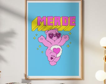 May include: A framed art print featuring a pink cartoon bear with heart-shaped sunglasses and a heart on its belly. The word "MERDE" is displayed in yellow and pink block letters against a light blue background.