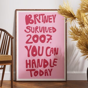 Pink Britney Spears wall art featuring the funny motivational quote “Britney Survived 2007, You Can Handle Today” in bold retro typography. This Y2K-inspired poster has dark pink lettering on a light pink background