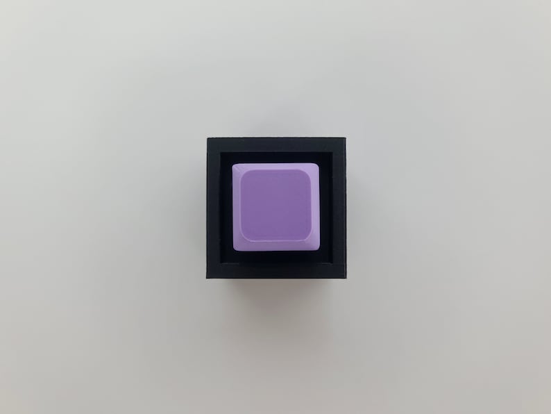 May include: A single purple keycap in a black keycap holder.