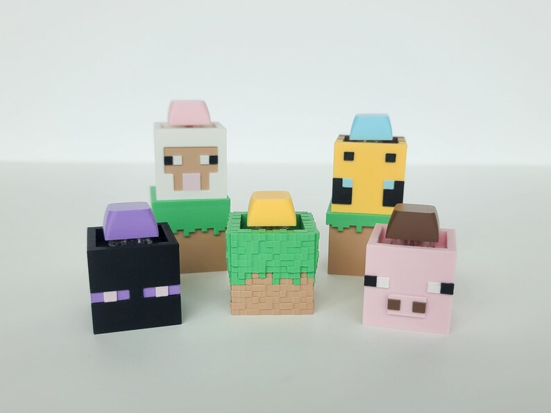 K&ouml;nnte beinhalten: F&uuml;nf Minecraft-Charakterfiguren mit verschiedenen Kopf- und K&ouml;rperfarben. Die Figuren sind ein Schaf, ein Schwein, eine Biene, ein Creeper und ein Steve. Jede Figur steht auf einem gr&uuml;nen Grasblock mit einem braunen Erdblock darunter.