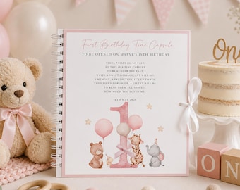 May include: A spiral-bound First Birthday Time Capsule book with a pink border, featuring a large number one, illustrations of a bear, giraffe, and elephant with balloons, and text reading To be opened on Maeve's 18th birthday, 16th May 2026.