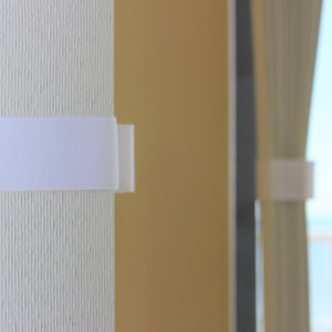 May include: White fabric window blinds with a white velcro strap to hold them in place.