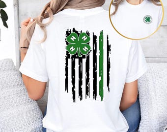 May include: White t-shirt with a distressed American flag design featuring a green 4-H clover in the top left corner. The back of the shirt has the text "4-H" on the clover.