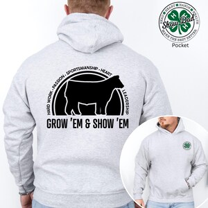 May include: A light grey hoodie featuring a black cow graphic within a circle, with the text "GROW 'EM & SHOW 'EM" beneath. The back of the hoodie also displays the words "HARD WORK. PASSION. SPORTSMANSHIP. HEART. LEADERSHIP." A small circular logo is on the upper right.