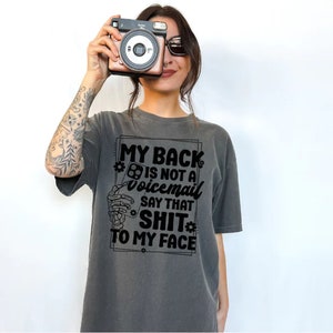 May include: A grey t-shirt with a black graphic that says "My back is not a voicemail say that shit to my face".