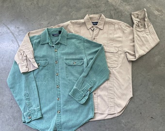 Puede incluir: Dos camisas de botones, una de color verde claro y otra de color beige. Ambas camisas tienen mangas largas y cierres de botones.
