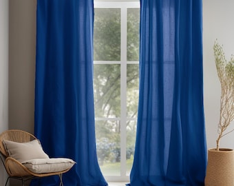 May include: Two blue linen curtains hanging in front of a window. The curtains are a deep blue color and have a textured, linen look.