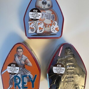May include: Three Star Wars themed metal tins. One tin features BB-8 with the text "BB&", another features Rey with the text "REY", and the last features Darth Vader with the text "VADER". Each tin has a sticker that says "€12, 47 CARDS + LIMITED EDITION + EPIC PATCH CARD".