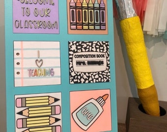 May include: A light blue classroom sign with six colorful squares featuring school-themed images and text. The text includes "WELCOME TO OUR CLASSROOM" and "TEACHING". A large pencil decoration is to the right.