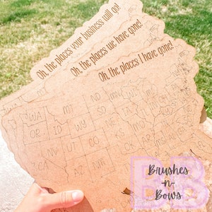 May include: A wooden map of the United States with the text "Oh, the places your business will go!" "Oh, the places we have gone!" and "Oh, the places I have gone!" written on it. The map is brown and has the state abbreviations written on it. The text "Brushes -n- Bows" is written in pink on a white background in the lower right corner of the image.