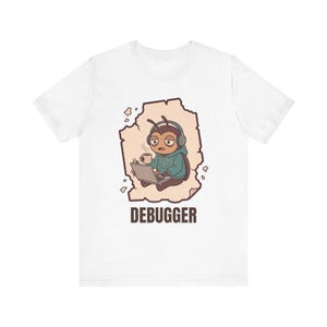 Könnte beinhalten: Ein weißes T-Shirt mit einer Grafik eines braunen Käfers, der Kopfhörer und einen blaugrünen Kapuzenpullover trägt, eine Kaffeetasse hält und an einem Laptop arbeitet. Unter der Illustration steht das Wort DEBUGGER in braunen Buchstaben.