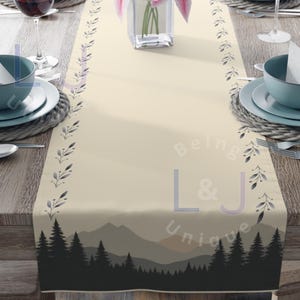 May include: A beige table runner with a forest silhouette design and a floral border. The text "Being L&J Unique" is printed on the runner.