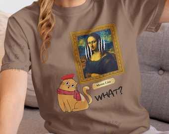 May include: A brown t-shirt featuring a humorous design. The design includes a framed parody of the Mona Lisa with white lines, a cartoon cat wearing a beret and scarf, and the word "WHAT?" below the cat.
