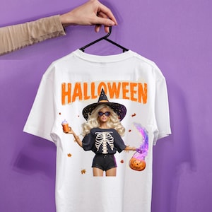 Puede incluir: Una camiseta blanca con el gráfico de una muñeca rubia que lleva un sombrero de bruja negro, gafas de sol y una camiseta negra con un estampado de caja torácica. La muñeca sostiene una taza naranja y una calabaza con humo mágico morado.