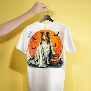 May include: A white t-shirt featuring a graphic print of a collie dog dressed as a ghost, sitting in front of a large orange moon. The dog is holding a pumpkin-shaped bucket filled with candy, surrounded by spiderwebs and flying bats.