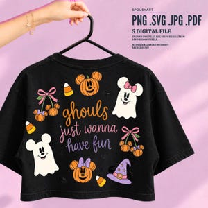 May include: A black t-shirt featuring a colorful Halloween-themed graphic with the text "ghouls just wanna have fun." The design includes illustrations of pumpkin heads with bows, white ghost figures, candy corn, and a purple witch hat.