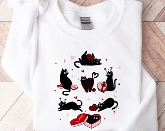 May include: White sweatshirt with a black cat design. The cats are holding hearts and some have a crown on their head. The text "Love" is on a heart-shaped box.