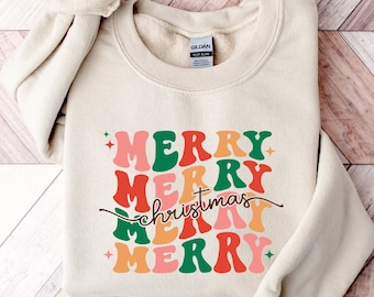 May include: A beige sweatshirt with a retro-style graphic design that says "Merry Christmas Merry" in red, green, orange, and pink.