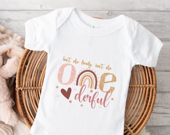 May include: White onesie with a pink and gold glitter 'one' with a rainbow and the text 'Isn't she lovely, isn't she deriful'.