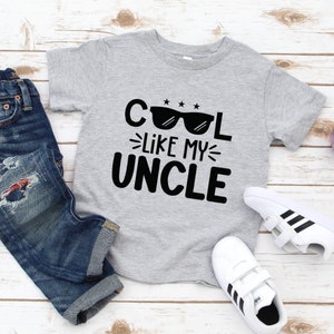 May include: A grey t-shirt with black text that reads "Cool Like My Uncle" with a pair of sunglasses above the word "Cool".