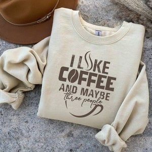 May include: A beige sweatshirt with the text "I like coffee and maybe three people" printed in brown. The text is stylized to look like a coffee cup with steam coming off the top.