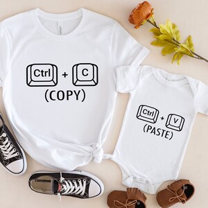 May include: White t-shirt with the text "Ctrl + C (COPY)" and a white onesie with the text "Ctrl + V (PASTE)".
