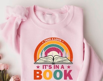 May include: A light pink sweatshirt with a graphic design featuring a rainbow, an open book, and the text "TAKE A LOOK IT'S IN A BOOK". The design has a vintage, retro style.