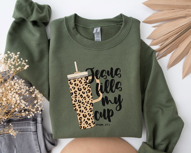 May include: Green sweatshirt with a leopard print tumbler and the text "Jesus fills my cup, Philippians 4:13".