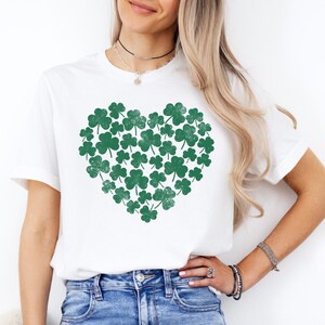 May include: White t-shirt with a green shamrock heart design. The shamrocks are arranged in a heart shape.