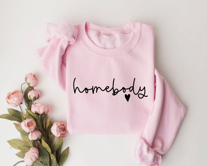 May include: A pink sweatshirt with the text "homebody" in black script with a small black heart.