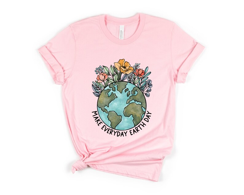 May include: A light pink t-shirt featuring a watercolor illustration of the Earth with flowers and the text "MAKE EVERYDAY EARTH DAY" in black. The shirt is made of a soft material and has rolled-up sleeves.