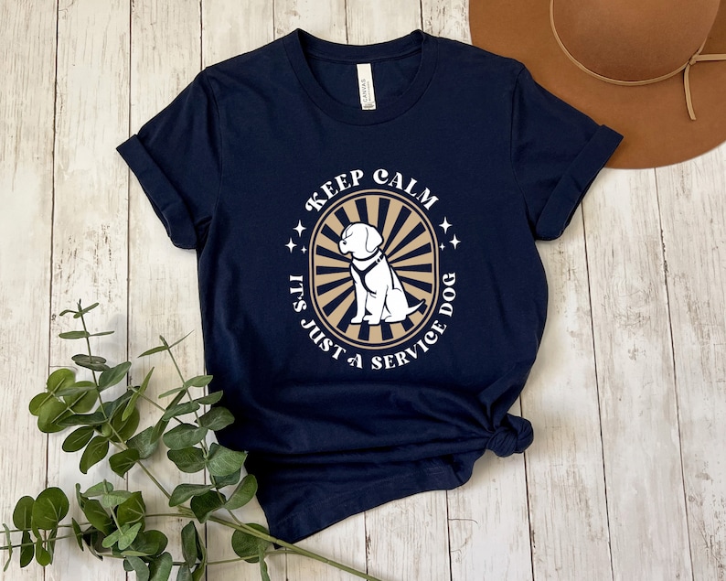 Peut inclure: T-shirt bleu marine avec un graphique blanc d'un chien dans un cercle avec le texte "Keep Calm It's Just a Service Dog".