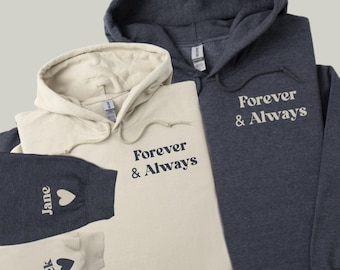 May include: Two hoodies, one in beige and one in navy blue, with the text "Forever & Always" printed on the front. The beige hoodie has a matching pair of sweatpants with the names "Jack" and "Jane" printed on the legs.