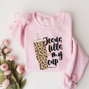 May include: Pink sweatshirt with a leopard print tumbler and the text "Jesus fills my cup, Psalm 23:5".