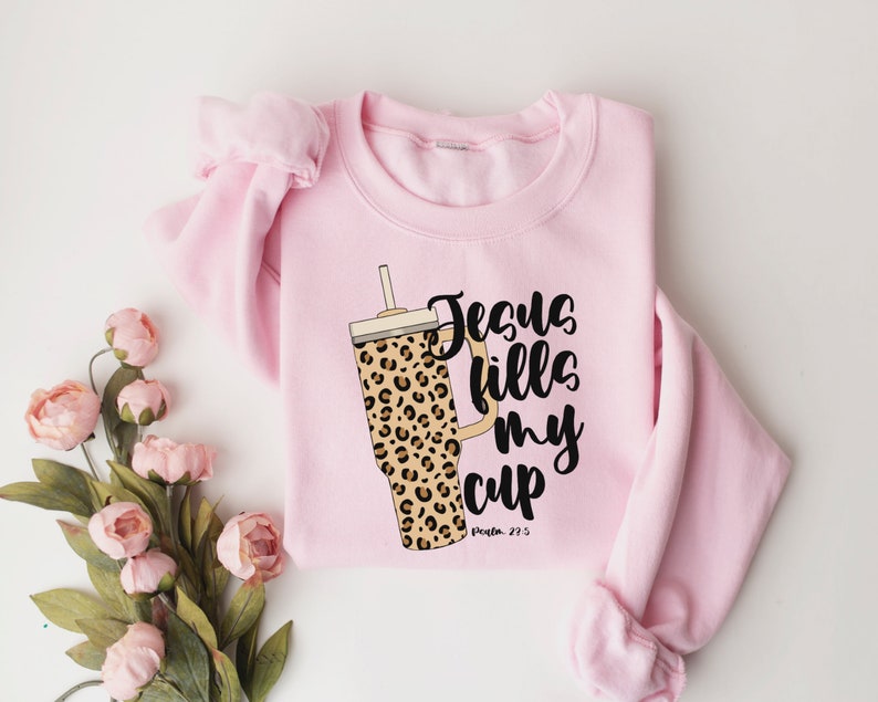 May include: Pink sweatshirt with a leopard print tumbler and the text "Jesus fills my cup, Psalm 23:5".