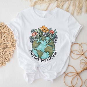 May include: White t-shirt featuring a watercolor illustration of Earth surrounded by flowers. The design includes the text "MAKE EVERYDAY EARTH DAY" in black. The shirt is made of a soft material and has short sleeves.