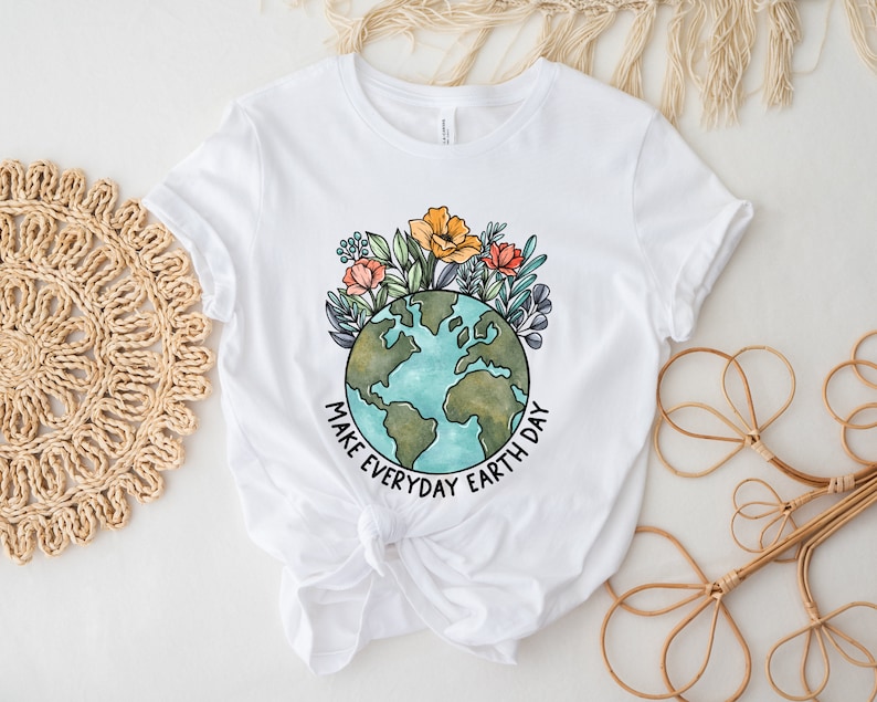 May include: White t-shirt featuring a watercolor illustration of Earth surrounded by flowers. The design includes the text "MAKE EVERYDAY EARTH DAY" in black. The shirt is made of a soft material and has short sleeves.