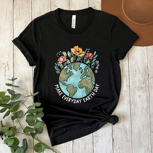 May include: Black t-shirt featuring a colorful illustration of the Earth surrounded by flowers and foliage. The text "MAKE EVERYDAY EARTH DAY" is printed in white. The shirt is made of a soft material.