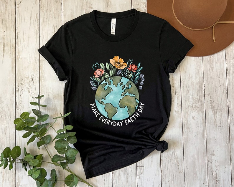 May include: Black t-shirt featuring a colorful illustration of the Earth surrounded by flowers and foliage. The text "MAKE EVERYDAY EARTH DAY" is printed in white. The shirt is made of a soft material.