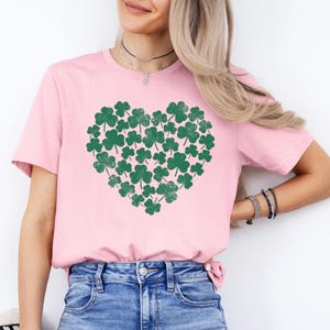 May include: A pink t-shirt with a green shamrock heart design. The shamrocks are arranged in a heart shape and have a distressed look.