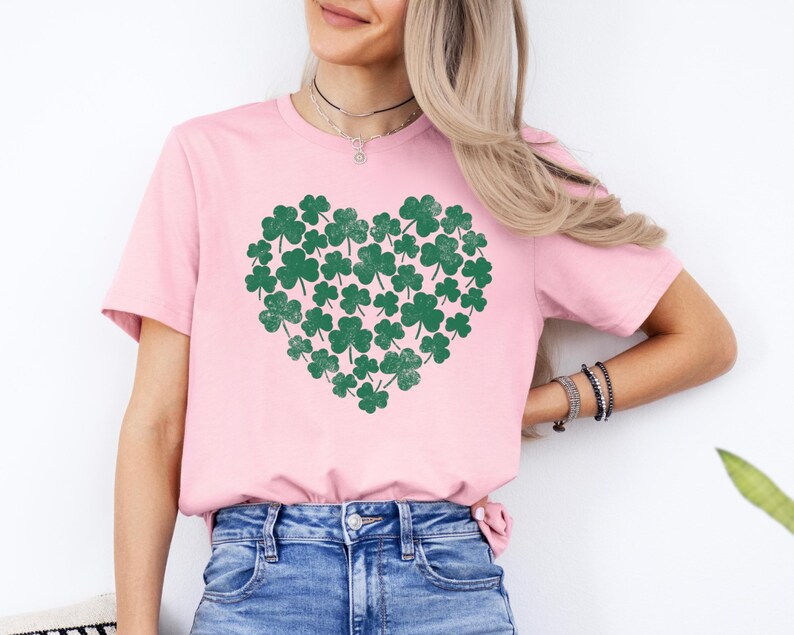 May include: A pink t-shirt with a green shamrock heart design. The shamrocks are arranged in a heart shape and have a distressed look.