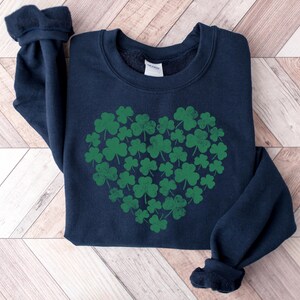 May include: A navy blue sweatshirt with a green shamrock heart design. The shamrocks are arranged in a heart shape and are a darker shade of green.