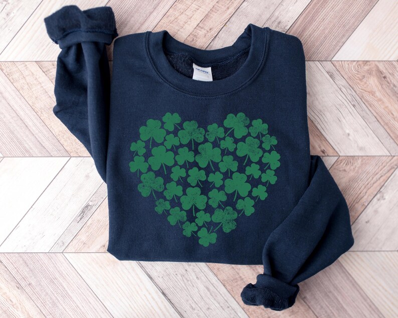 May include: A navy blue sweatshirt with a green shamrock heart design. The shamrocks are arranged in a heart shape and are a darker shade of green.