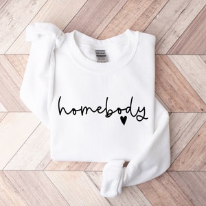 May include: White sweatshirt with the text "homebody" in black script with a small black heart.