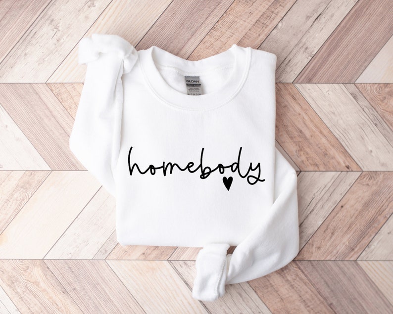 May include: White sweatshirt with the text "homebody" in black script with a small black heart.