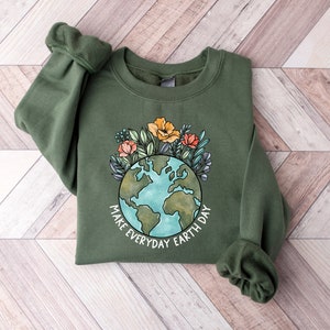 May include: An olive green sweatshirt featuring a watercolor design of the Earth surrounded by flowers. The text "MAKE EVERYDAY EARTH DAY" is printed below the globe. The sweatshirt has long sleeves and a crew neck.