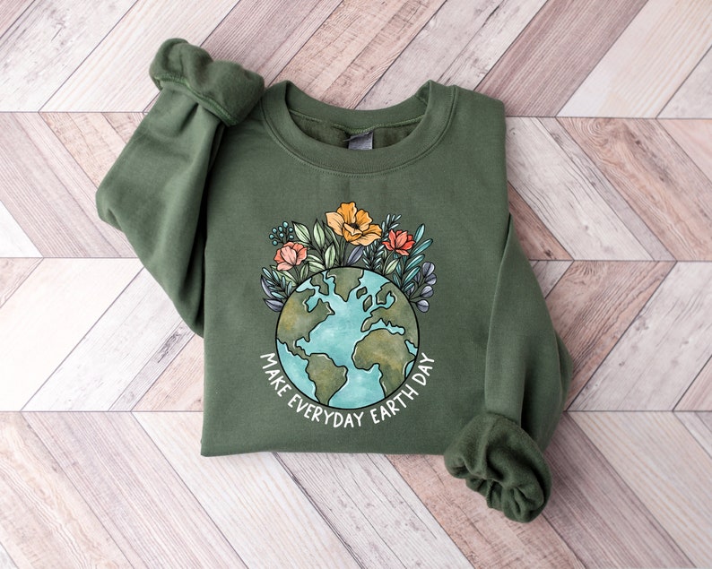 May include: An olive green sweatshirt featuring a watercolor design of the Earth surrounded by flowers. The text "MAKE EVERYDAY EARTH DAY" is printed below the globe. The sweatshirt has long sleeves and a crew neck.