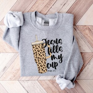 May include: Gray sweatshirt with a leopard print tumbler and the text "Jesus fills my cup, Psalm 23:5".