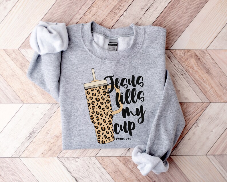 May include: Gray sweatshirt with a leopard print tumbler and the text "Jesus fills my cup, Psalm 23:5".