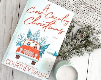 May include: A book cover with a red truck carrying a Christmas tree, with the title "A Cross-Country Christmas" and the author's name "Courtney Walsh".